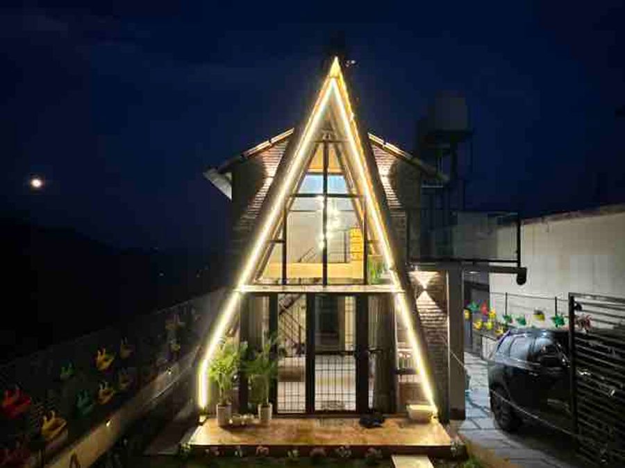 Illuminated A-frame chalet facade glowing against the night sky in Bhimtal