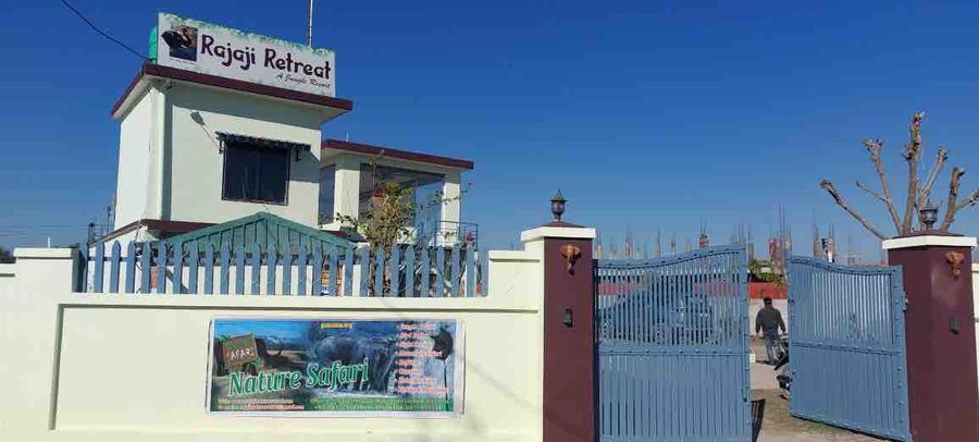 Resort entrance gate with perimeter wall and property signboard under a clear blue sky in Rishikesh