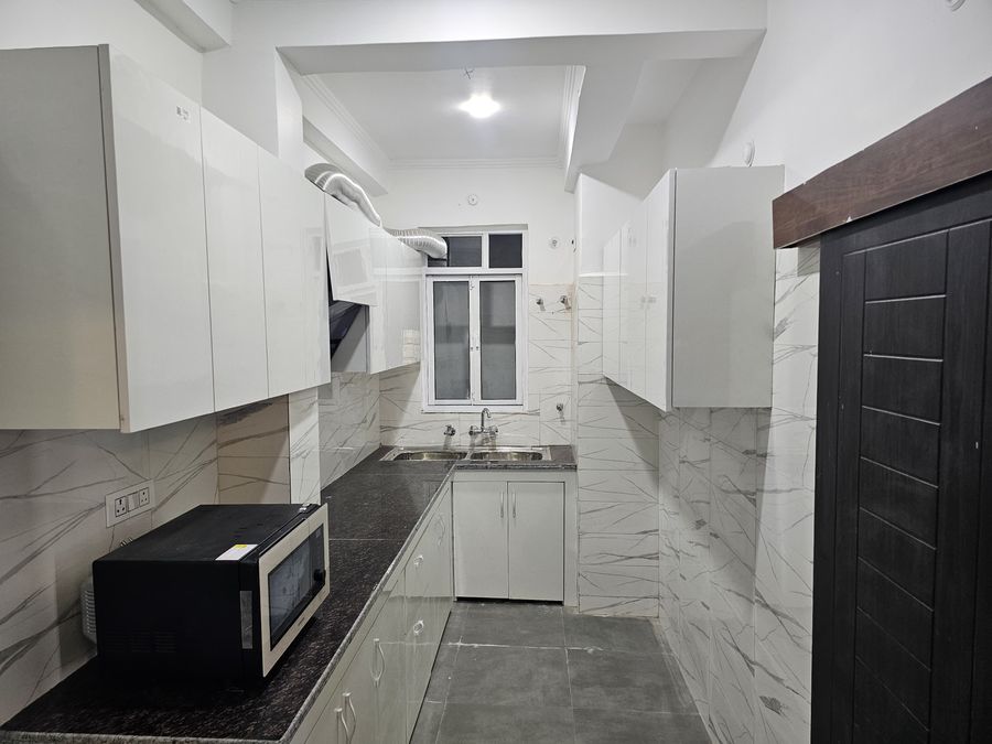 Fully equipped modular kitchen with white cabinets, countertop, and microwave in Rishikesh