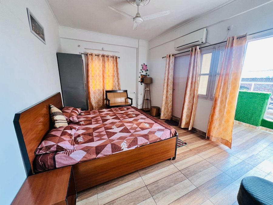 Sunlit bedroom featuring a wooden double bed, wardrobe, and balcony access in Rishikesh