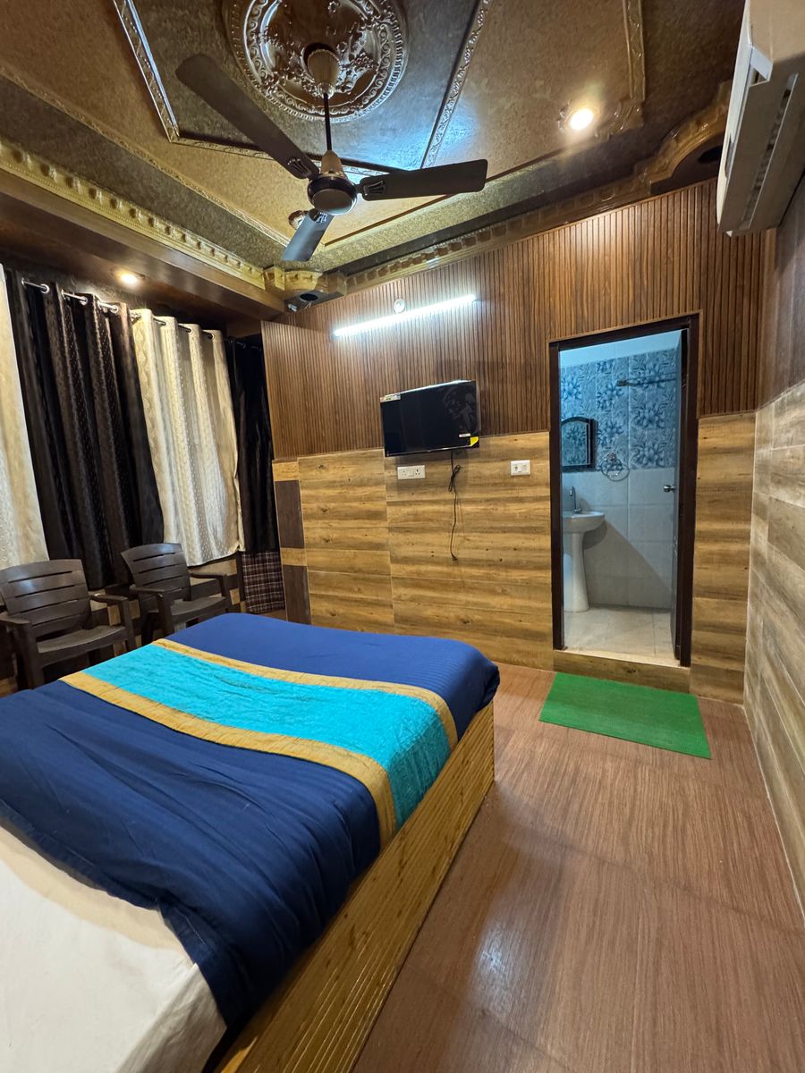Cozy double bedroom featuring wood-clad walls, wall-mounted TV, and attached bath entrance in Rishikesh