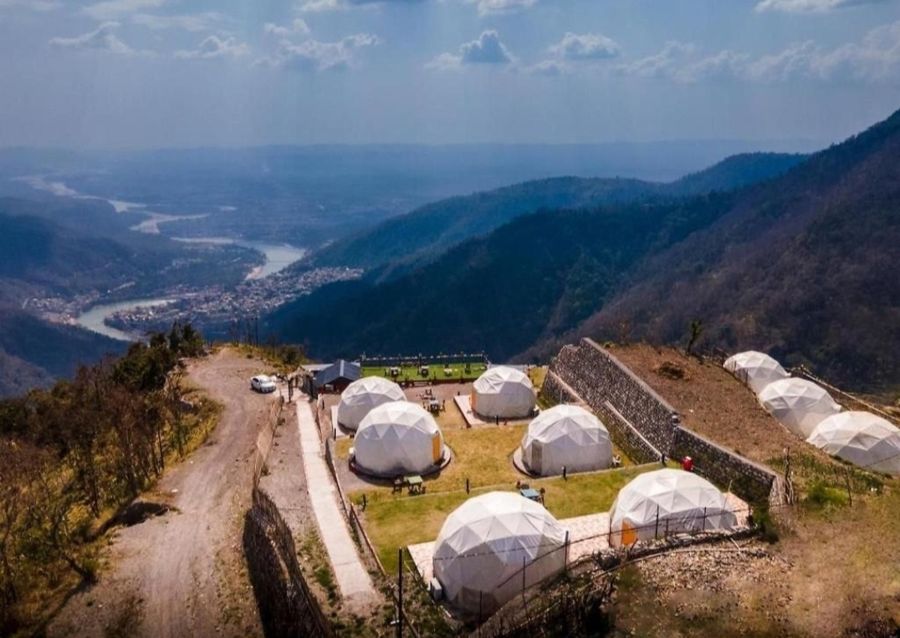 High-angle panoramic vista of luxury dome campsite perched above the winding river valley in Rishikesh