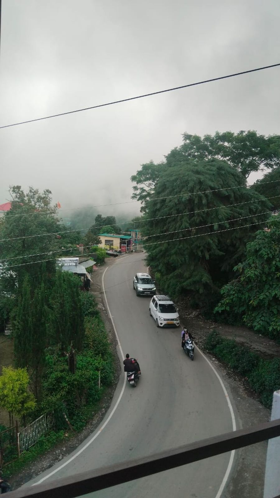 Hillside road and lush forest landscape viewed from balcony in Bhimtal