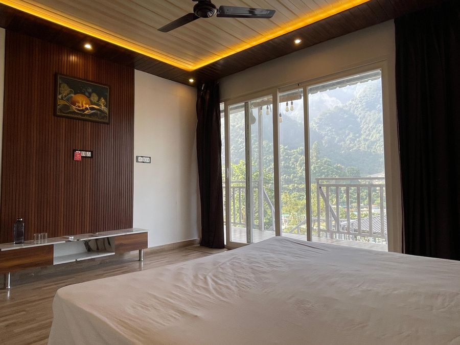 Well-appointed bedroom featuring accent wood paneling and panoramic balcony windows in Rishikesh