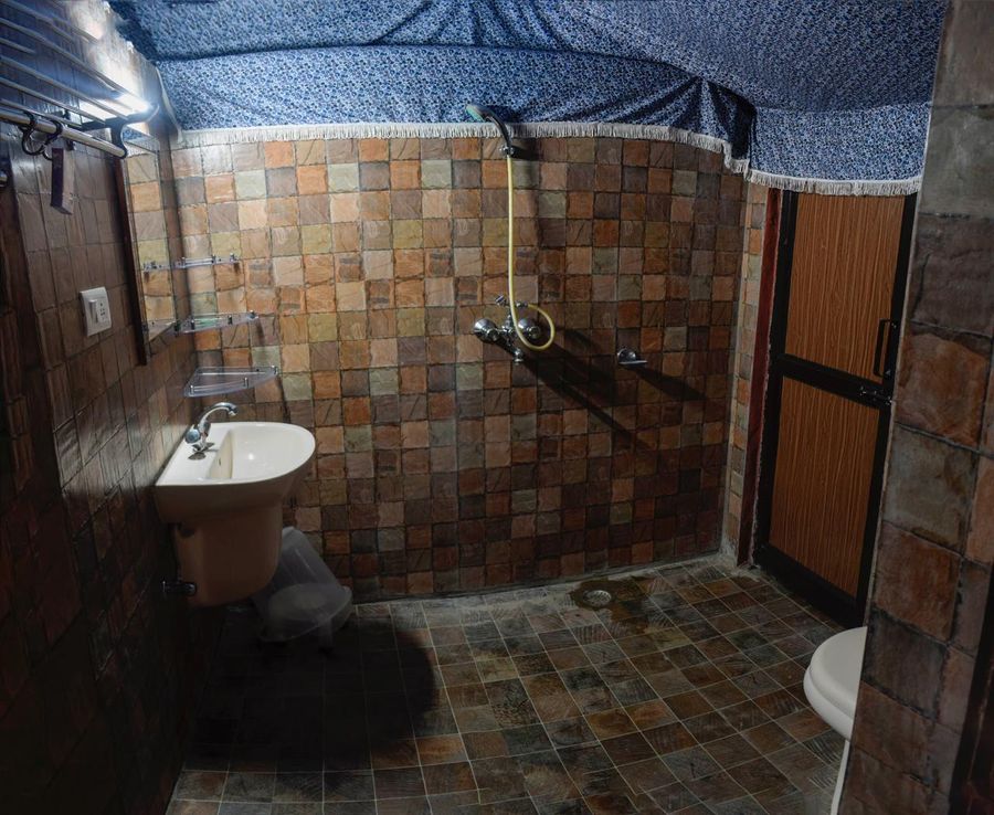 Tiled campsite washroom fitted with a pedestal sink and shower fixtures in Rishikesh