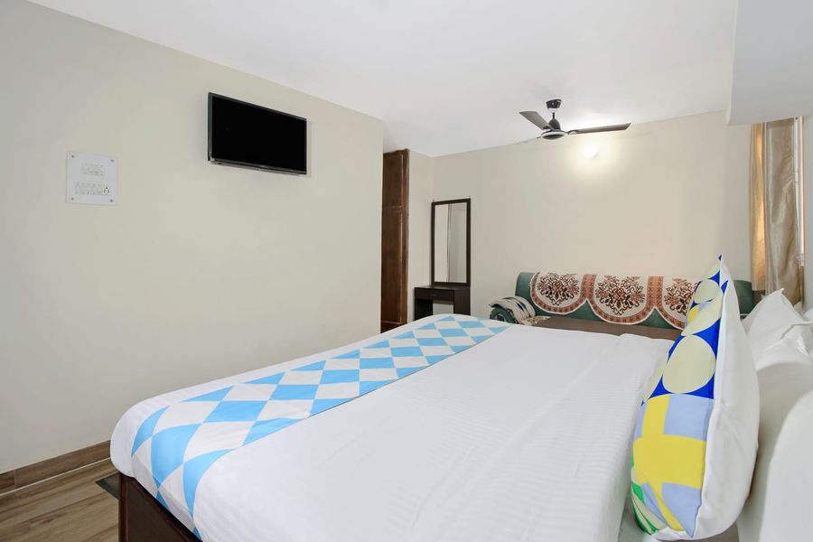 Well-lit bedroom with wall-mounted TV and vanity mirror in Bhimtal
