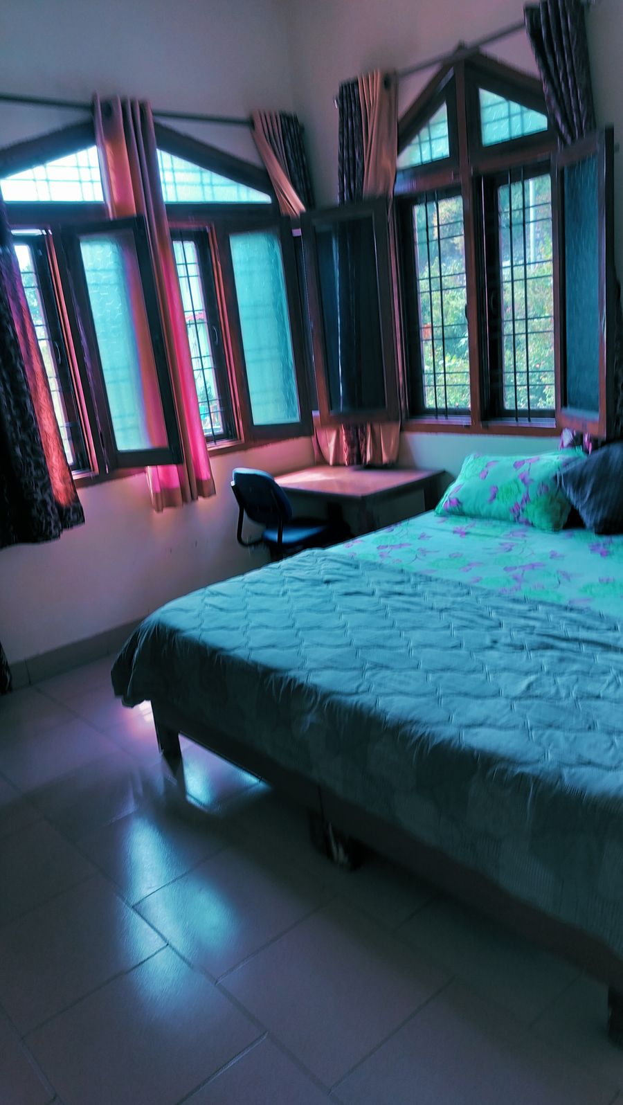 Sunlit guest room setup with study chair and green bedcover in Bhimtal