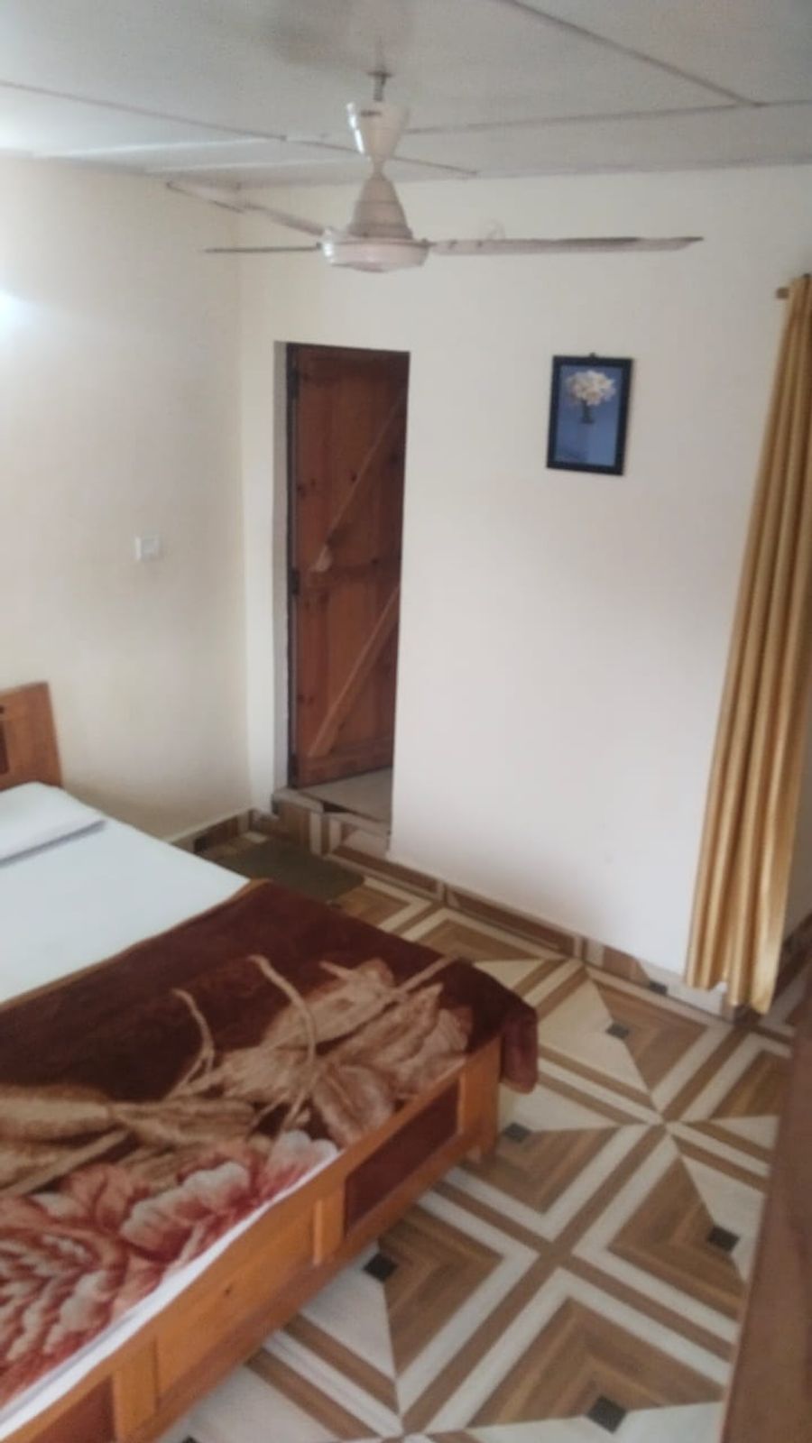 Simple bedroom with double bed and attached wooden door entryway in Bhimtal