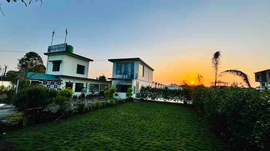 Sprawling garden lawn with resort buildings outlined against a sunset sky in Rishikesh
