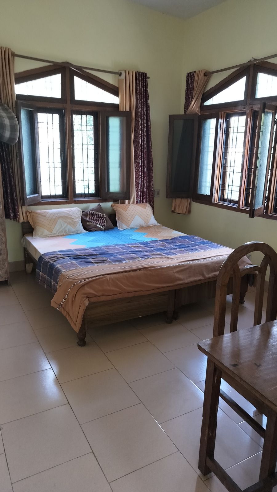 Bright bedroom with wooden double bed and multi-pane windows in Bhimtal