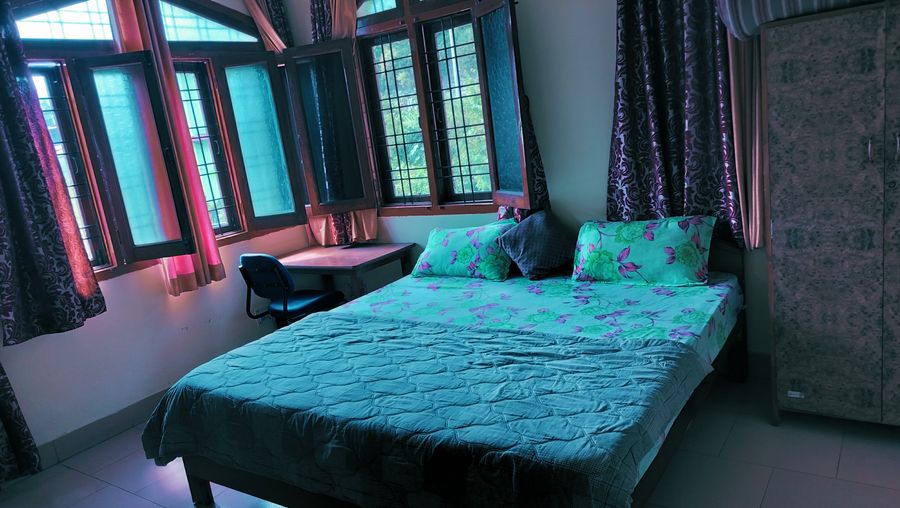 Cozy bedroom featuring teal bedding, study desk, and large windows in Bhimtal