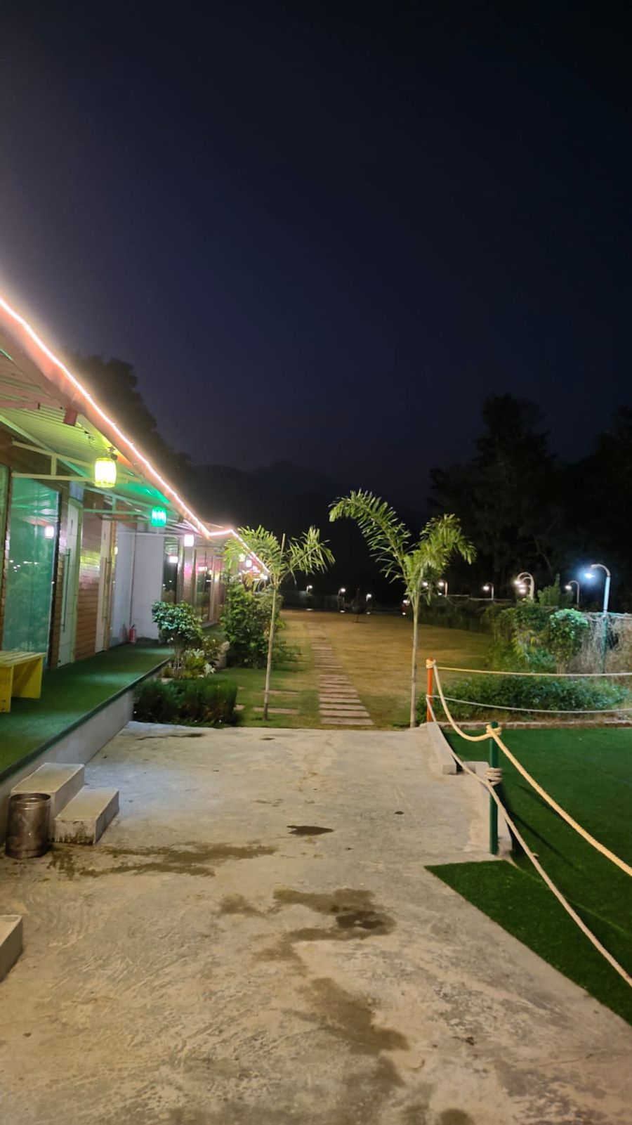 Evening view of the cottage walkway and open lawn illuminated by warm lights in Rishikesh
