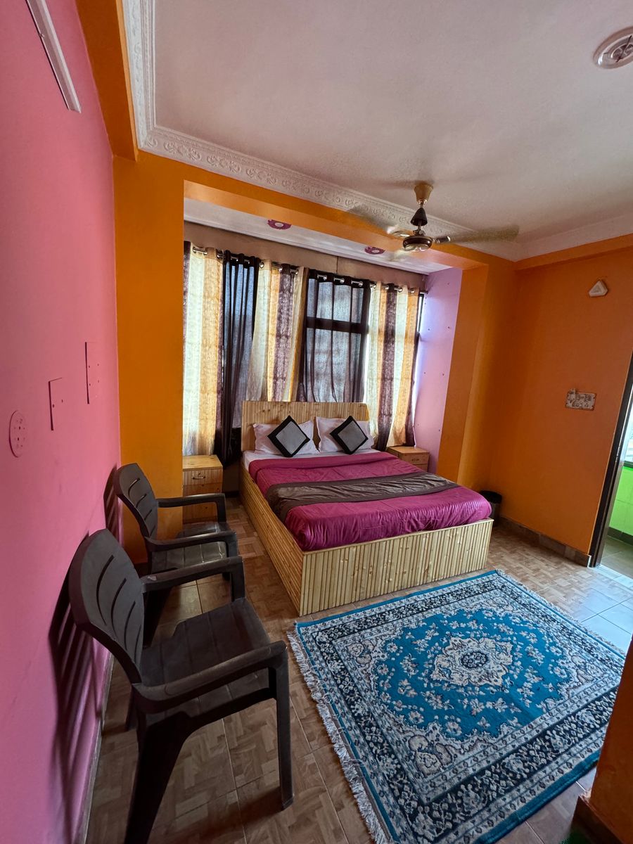 Warm orange bedroom setup with double bed, armchair, and tall windows in Rishikesh