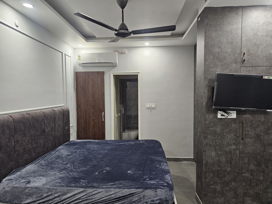 Contemporary air-conditioned bedroom with dark accent wall paneling and TV in Rishikesh