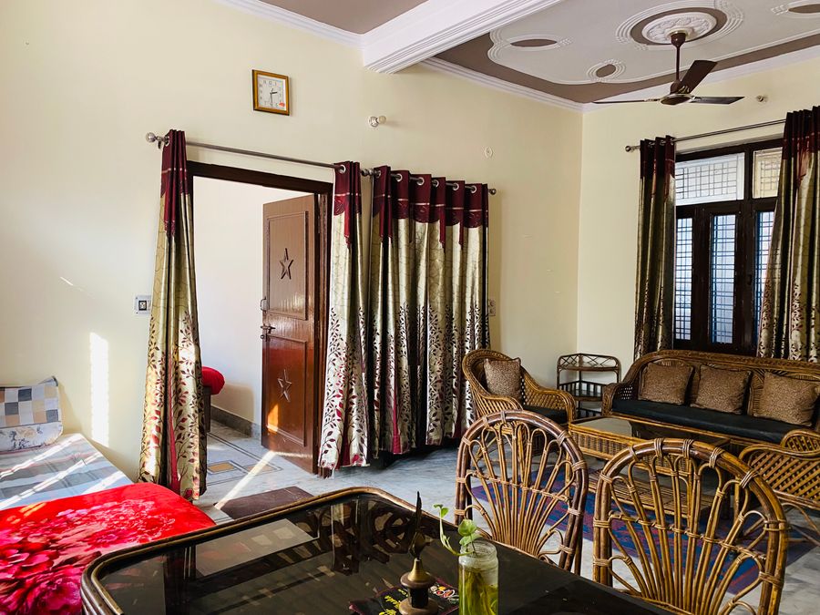 Sunlit living and dining hall featuring cane chairs, wooden furniture, and window drapes in Rishikesh