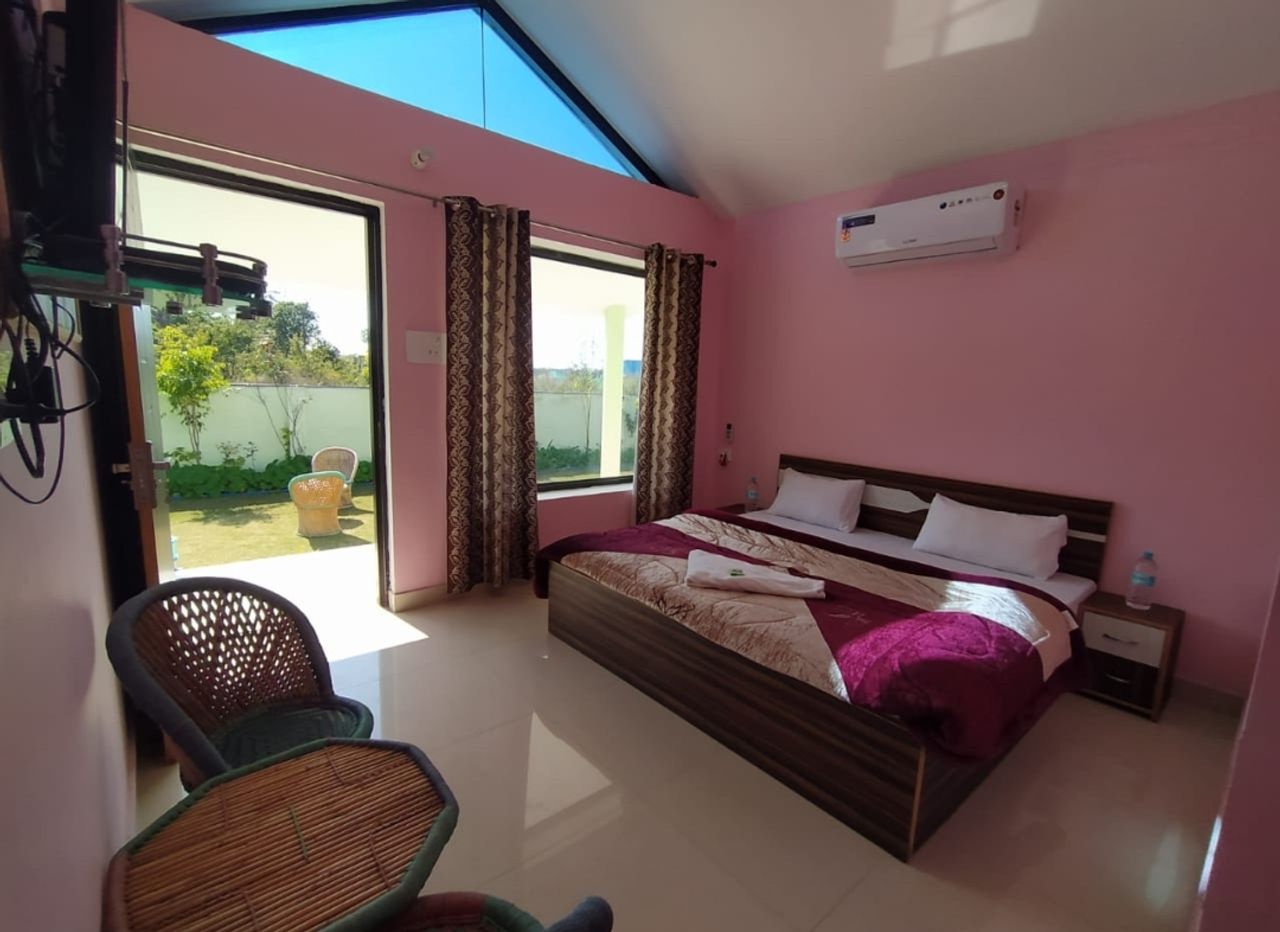 Bright cottage bedroom interior featuring pastel walls, a double bed, cane seating, and garden access in Rishikesh