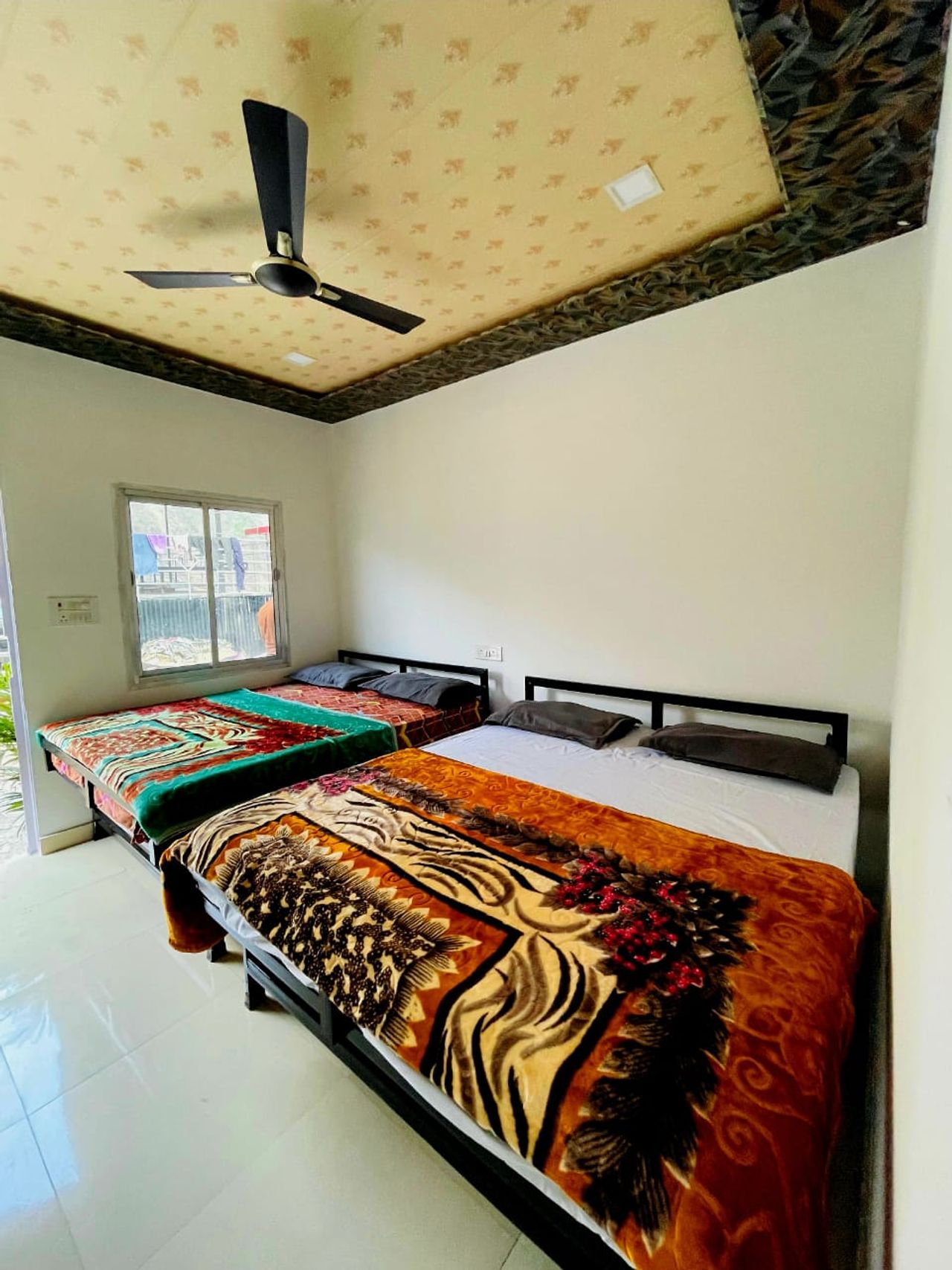Sunlit bedroom featuring multiple double beds and patterned blankets in Rishikesh