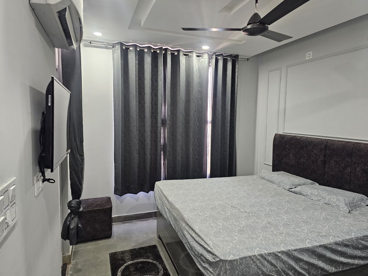 Minimalist bedroom suite with upholstered headboard, double bed, and full-length drapes in Rishikesh