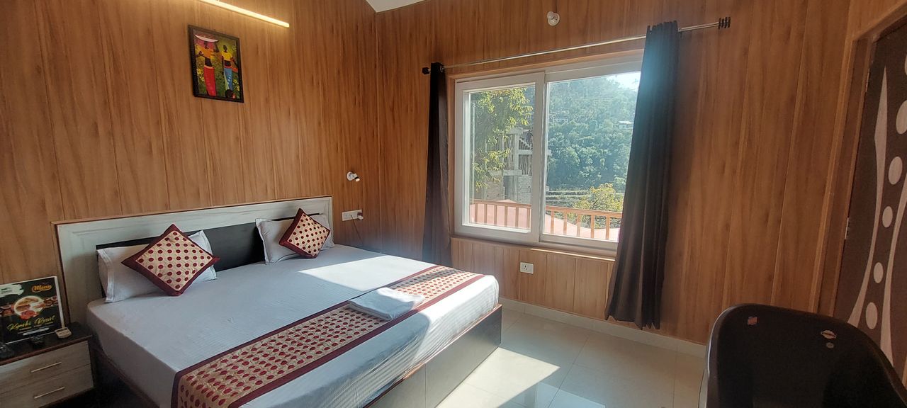 Wood-paneled guest room with double bed and window framing mountain landscapes in Rishikesh